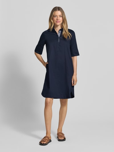 Frauenmodel trägt knielanges Hemdblusenkleid mit Eingrifftaschen von Christian Berg Woman aus reiner Baumwolle in Dunkelblau, gerader Schnitt, verdeckte Knopfleiste, 1/2-Arm, Ganzkörperansicht von vorne.