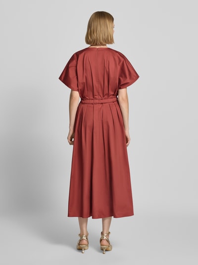 Frauenmodel trägt Cocktailkleid mit V-Ausschnitt und Schnürung von Christian Berg Cocktail in Ziegelrot, A-Linie, Midikleid, Rückansicht.