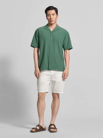 Männermodel trägt Regular Fit Freizeithemd mit Reverskragen von MCNEAL in grün, Material-Mix mit Stretch-Anteil, fein strukturiert, Knopfleiste, dazu helle Shorts und Sandalen, Ganzkörperansicht von vorne.