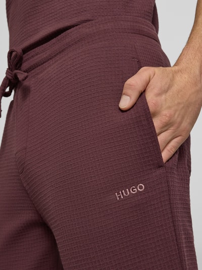 Männermodel trägt Relaxed Fit Pyjama-Hose aus Baumwoll-Mix Modell 'AUSTIN PANTS' von HUGO in Unifarben mit Waffel-Struktur, Label-Print, Tunnelzug und seitlichen Eingrifftaschen, Regular-Fit Passform; Nahaufnahme Oberkörper.