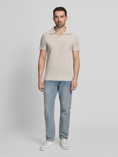 Männermodel trägt Relaxed Fit Poloshirt mit V-Ausschnitt von Lindbergh aus Baumwoll-Mix in Beige mit Frottee, Brusttasche, Ganzkörperansicht von vorne.