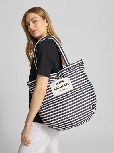 Frauenmodel trägt Handtasche mit Steppnähten und Label-Detail von MADS NØRGAARD, schwarz-weiß gestreift, Stoff mit Tragehenkel, Ganzkörperansicht Rückansicht.