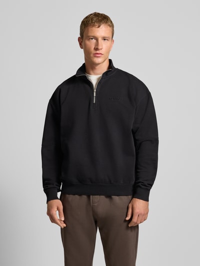 Męski model nosi Oversized Sweatshirt mit Stehkragen od Pegador, mieszanka bawełny, prążkowane wykończenia, haftowane logo, zamek błyskawiczny, długość tyłu 67 cm, długość rękawa 61 cm, krój oversized, kolor czarny, widok z przodu, ujęcie całej sylwetki.