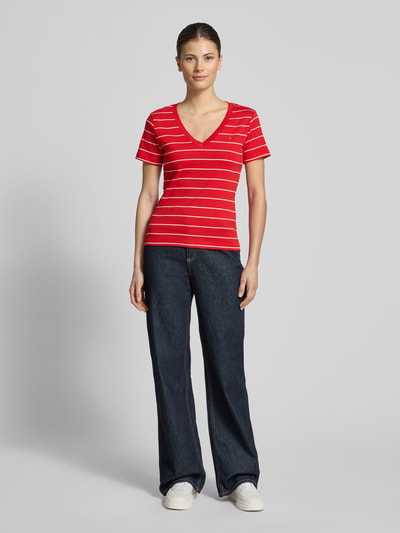 Vrouwenmodel draagt Slim Fit T-Shirt aus reiner Baumwolle van Tommy Hilfiger, rood-wit gestreept, jersey, logo detail, v-hals, korte mouw, two tone look, ganzlichaamsaanzicht van voren.