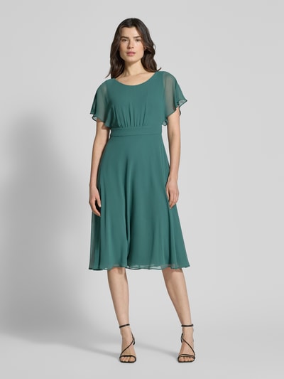 Frauenmodel trägt Knielanges Kleid mit Rundhalsausschnitt von Vera Mont in Grün, semitransparent, tailliert, blickdichter Unterrock, Ganzkörperansicht von vorne.