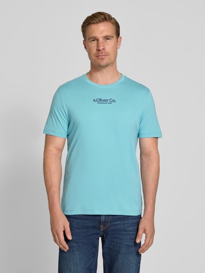 Męski model nosi Regular Fit T-Shirt aus reiner Baumwolle von s.Oliver RED LABEL w kolorze jasnoniebieskim, krój regular fit, jednokolorowa optyka, okrągły dekolt, krótki rękaw, materiał jersey z czystej bawełny, detal z logo na piersi, widok całej sylwetki z przodu.