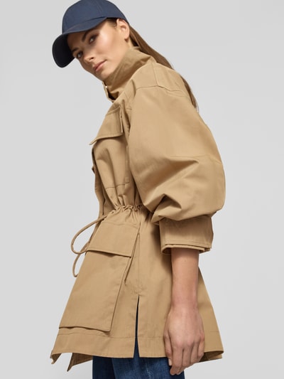 Modelka kobieca nosi Jacke mit Stehkragen und Pattentaschen od Jake*s Casual, beżowy kolor, bawełniany miks, krój taliowany, długość tyłu 75 cm, szerokość ramion 58 cm, szerokość w biuście 42 cm, długość rękawa 56 cm, duże kieszenie, widok całej sylwetki z przodu.