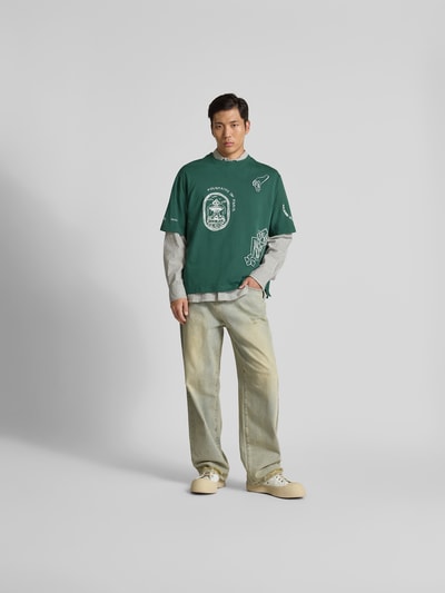 Männermodel trägt Oversized T-Shirt aus Bio-Baumwolle von MAISON KITSUNÉ in Grün mit Label-Print, gerippter Rundhalsausschnitt, Ganzkörperansicht von vorne.