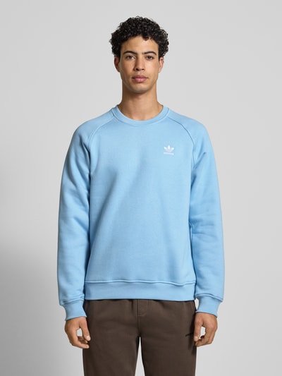 Männermodel trägt Sweatshirt mit Label-Stitching von adidas Originals in Hellblau, Baumwoll-Mix, lockerer Schnitt, gerippte Abschlüsse, Rundhalsausschnitt, Ganzkörperansicht von vorne.