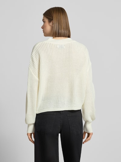 Vrouwenmodel draagt Regular Fit Strickjacke mit einreihiger Knopfleiste Modell 'CAROL NICE' van Only in effen gebreide look, cropped, met label stitching, diepe V-hals en lange mouw, geribde zooms, detailopname van achteraan.