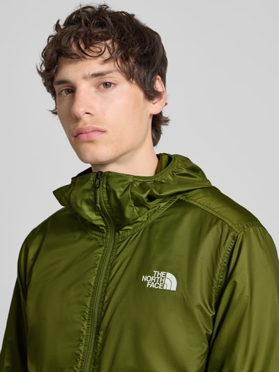 Männermodel trägt Windbreaker mit Logo und Reißverschlusstaschen von The North Face in regular fit, olivgrün, Nahaufnahme Oberkörper