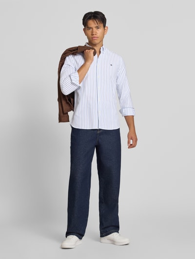 Männermodel trägt Regular Fit Freizeithemd mit Logo-Stitching von Superdry, Weiß mit blauen Streifen, reine Baumwolle, Ganzkörperansicht von vorne. Rückenlänge 73 cm, Schulterbreite 40 cm, Ärmellänge 63 cm, Button-Down-Kragen, Knopfleiste, Sportmanschetten.