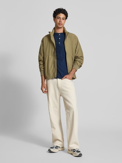 Männermodel trägt T-Shirt mit kurzer Knopfleiste von Superdry in Dunkelblau, Baumwoll-Mix mit Leinen, Regular Fit, Polokragen, Logo-Stitching, kombiniert mit heller Hose; Ganzkörperansicht von vorne.