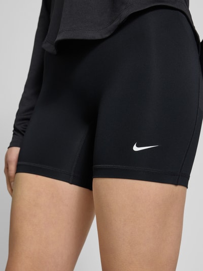 Frauenmodel trägt Radlerhose mit elastischem Bund und Logo von NIKE TRAINING, schwarz, körpernaher Schnitt, Logo vorn, Nahaufnahme Oberkörper.