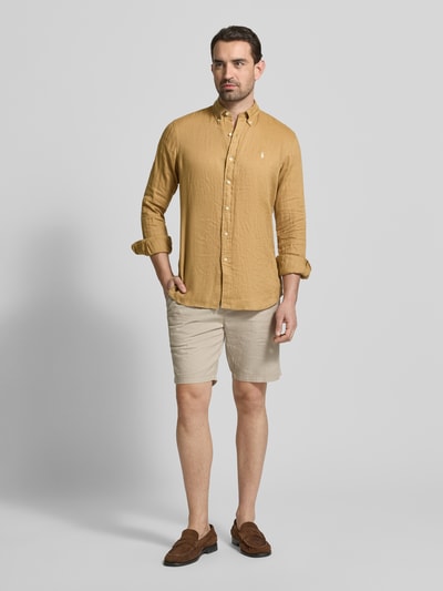 Mannelijk model draagt Regular Fit Freizeithemd aus reinem Leinen van Polo Ralph Lauren in effen lichtbruin, textuur van flammé linnen, logodetail, met knopenlijst en button-down kraag, lange mouwen met sportmanchet, licht afgeronde zoom, vooraanzicht volledige lichaamsopname.