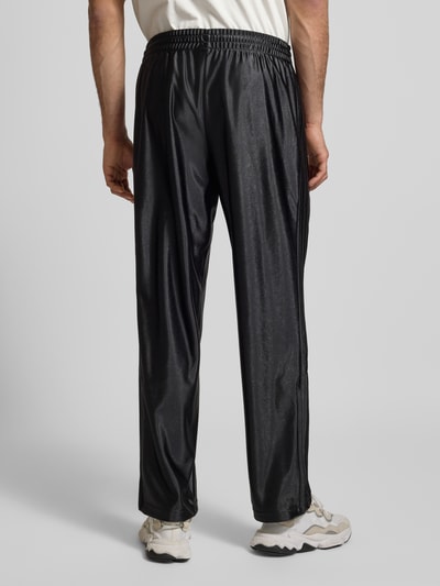 Mężczynamodel nosi spodnie treningowe z logo, model 'FIREBIRD' od adidas Originals, krój regular fit, elastyczny pas, czarna tkanina, długość wewnętrzna 79 cm, rozmiar M, zdjęcie całej sylwetki z tyłu.