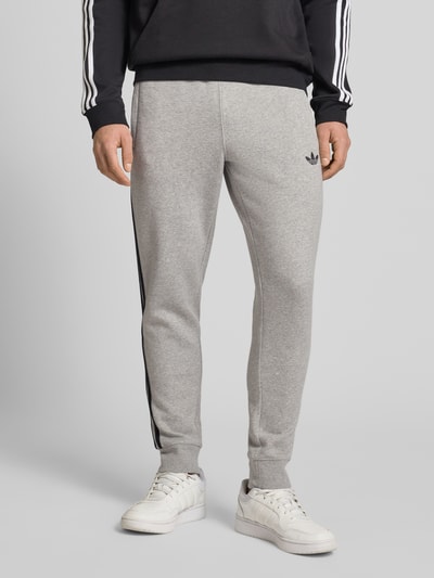 Mannenmodel draagt Sweatpants mit elastischem Bund van adidas Originals, grijs, katoenmix, los vallende fit, vooraanzicht, detailopname onderlichaam.