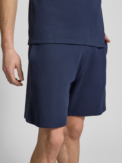 Mężczyznmodel nosi Szorty z elastycznym pasem od Christian Berg Men, mieszanka bawełny z dodatkiem streczu, luźny krój, tunel, kolor granatowy, szerokość w pasie 43 cm, długość wewnętrzna 19 cm, widok z przodu, zbliżenie na dolną część ciała.