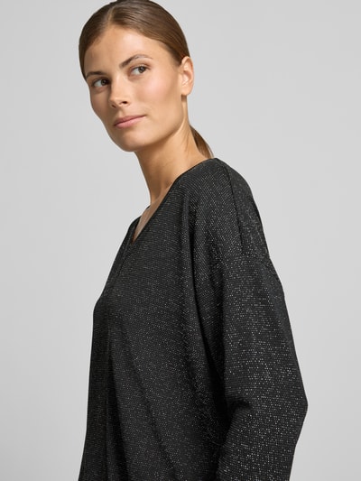 Vrouwenmodel draagt 3/4-Shirt met schimmerende optiek van VERO MODA, zwarte jersey, V-hals, licht afgeronde zoom, close-up van bovenlichaam.