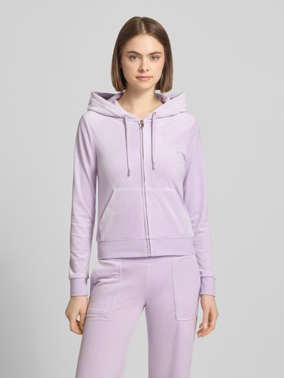 Frauenmodel trägt Slim Fit Sweatjacke aus Samt Modell 'Robertson' von Juicy Couture, Elastischer-Material-Mix, Kapuze mit Tunnelzug, Reißverschluss, geteilte Känguru-Tasche, elastische Abschlüsse, fliederfarbene Oberfläche, glatte Samt-Textur, Ganzkörperansicht von vorne.