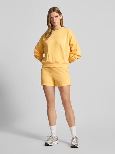 Kobiece modelka ma na sobie Shorts mit Logo und elastischem Bund od adidas Sportswear, żółty kolor, regular fit, bawełniany miks, logo, przedni widok całej sylwetki.
