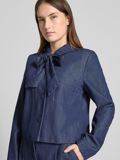 Vrouwenmodel draagt Regular Fit Blazer in denim-look met lyocell van Christian Berg Woman Selection, lang mouwen, blousekraag, sierstrik, knoopsluiting, getailleerde pasvorm, katoenmix, kleur blauw, textuur glad, borstzakken, close-up bovenlichaam.