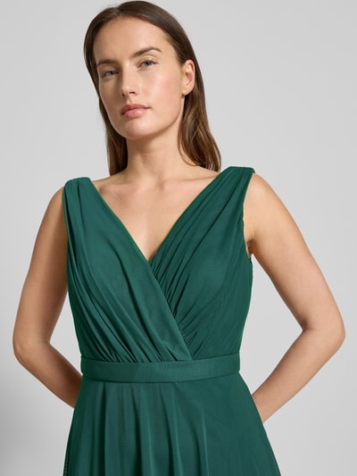 Frauenmodel trägt Cocktailkleid mit V-Ausschnitt von TROYDEN COLLECTION in Dunkelgrün, taillierter Schnitt, Raffungen, Nahaufnahme Oberkörper.