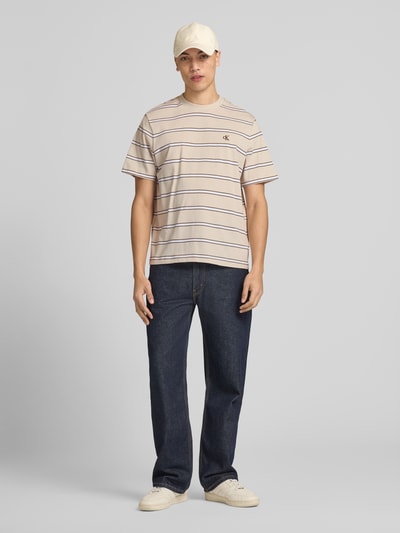 Männermodel trägt T-Shirt mit Logo-Stitching von Calvin Klein Jeans, reine Baumwolle, Gerader-Schnitt, Rundhalsausschnitt, Ganzkörperansicht von vorne.