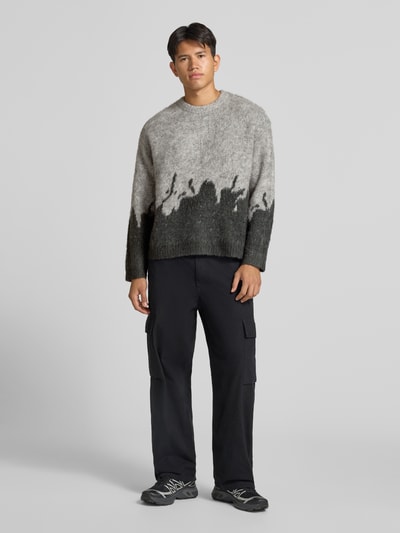 Männermodel trägt Strickpullover mit gerippten Abschlüssen von ANOTHER COTTON LAB, grauschwarze Farbverläufe, Ganzkörperansicht von vorne, elastischer Material-Mix mit Lanawoll-Anteil, gerader Schnitt, Rundhalsausschnitt, überschnittene Ärmel, Rückenlänge 62 cm, Ärmellänge 67 cm.