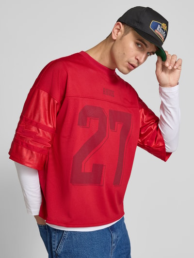 Männermodel trägt Basecap mit Label-Patch von RHUDE, Material-Mix mit Baumwoll-Anteil, Kontrastbesatz aus Denim, Nahaufnahme Oberkörper.