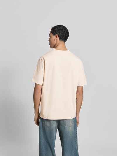 Männermodel trägt Relaxed Fit T-Shirt mit Brusttasche von MAISON KITSUNÉ aus reiner Baumwolle, dezentes Beige, Rückenansicht, Ganzkörperansicht Rückansicht.