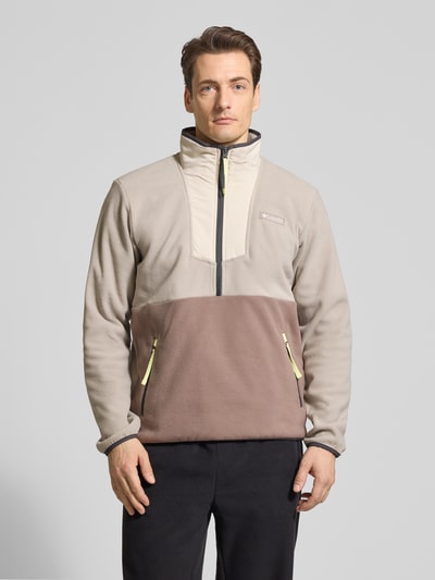 Männermodel trägt Fleecepullover mit Stehkragen und Reißverschluss von Columbia in Beige und Braun mit Label-Patch, Regular-Fit, Reißverschlusstaschen, Rückenlänge 70 cm, Ärmellänge 67 cm, Ganzkörperansicht von vorne.