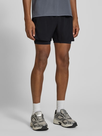 Männermodel trägt schwarze Shorts im 2-in-1-Look mit Logo von ASICS, elastischer Bund, Regular Fit, Bundweite 35 cm, Ganzkörperansicht von vorne.