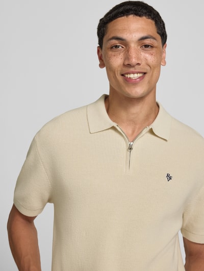 Mężczyzna nosi Boxy Fit Poloshirt mit Logo-Stitching od REVIEW z bawełny, kołnierzykiem polo, krótkim zamkiem błyskawicznym, kremowy, z wyhaftowanym logo, długość tyłu w rozmiarze M: 67 cm, bliska perspektywa górnej części ciała.