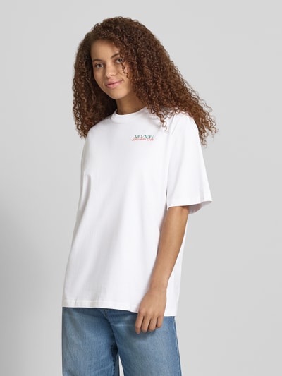 Frauenmodel trägt T-Shirt mit rückseitigem Motiv-Print von REVIEW in Weiß, oversized, Reine Baumwolle, Rundhalsausschnitt, Ganzkörperansicht von vorne.