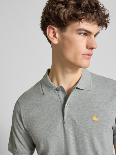 Männermodel trägt Regular Fit Poloshirt mit Label-Stitching von Carhartt Work In Progress, graue Baumwolle, Polokragen, Nahaufnahme Oberkörper.