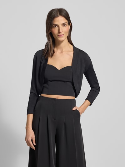 Frauenmodel trägt Bolero mit Schalkragen von Jake*s Cocktail aus schimmernder Viskosemischung mit gerippten Abschlüssen und Dreiviertel-Ärmeln, offene Vorderseite, Rückenlänge 39 cm bei Größe 36, Ganzkörperansicht von vorne.