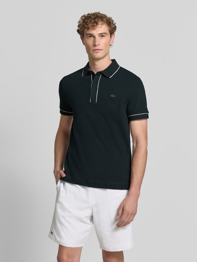 Männermodel trägt schwarzes Regular Fit Poloshirt aus Baumwoll-Mix Modell 'CHEMISE' von Lacoste, Herren Poloshirt, Ganzkörperansicht von vorne.