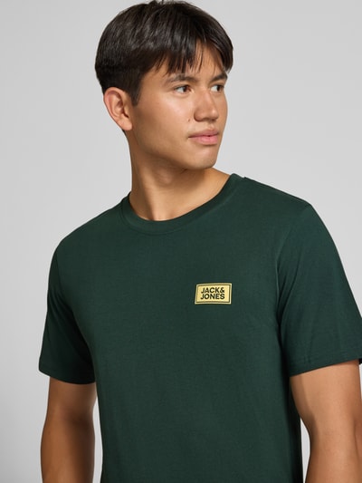 Männermodel trägt Regular Fit T-Shirt aus reiner Baumwolle mit Label-Detail von JACK & JONES in Dunkelgrün, Nahaufnahme Oberkörper.