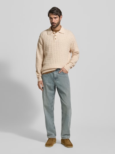 Männermodel trägt Strickpullover mit Strukturmuster Modell 'Gustav' von Les Deux, heller Farbton, Material-Mix mit Woll-Anteil, Regular-Fit, Polokragen und Knopfleiste, kombiniert mit hellblauer Jeans, Ganzkörperansicht von vorne.