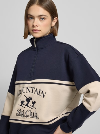Frauenmodel trägt Sweatshirt mit Reißverschluss Modell 'Cosette' von LeGer by Lena Gercke in Dunkelblau-Beige, Struktur-Stitching, Nahaufnahme Oberkörper.