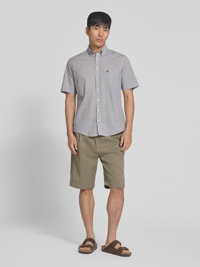 Männermodel trägt Modern Fit Freizeithemd mit borstzak en gestikt logo van Fynch-Hatton van puur katoen, button-downkraag, knoopsluiting, borstzak, afgeronde zoom, ruglengte maat M 73 cm, schouderbreedte maat M 40 cm, mouwlengte maat M 26 cm, grijs, groene korte broek, sandalen, lichte achtergrond. Ganzkörperansicht von vorne.