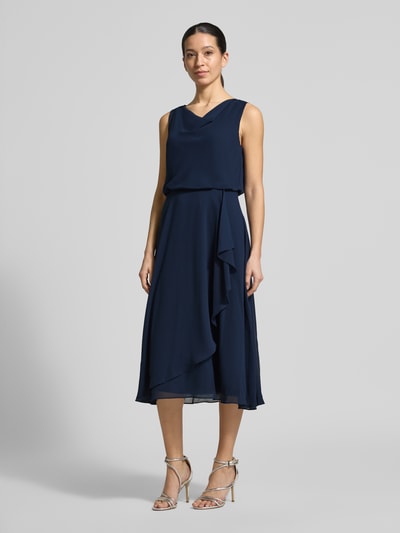 Frauenmodel trägt knielanges Cocktailkleid mit Wasserfall-Ausschnitt von Christian Berg Cocktail aus dunkelblauem Chiffon, Taillierter Schnitt, Breite Träger, Saum in Wickeloptik, rückseitiger Haken- und Reißverschluss, Rückenlänge 120 cm, Brustweite 45 cm, Ganzkörperansicht von vorne.