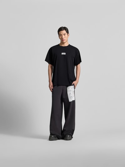Männermodel trägt Relaxed Fit T-Shirt mit Logo-Detail von MM6 Maison Margiela, reine Baumwolle, schwarz, Rundhalsausschnitt, Ganzkörperansicht von vorne.