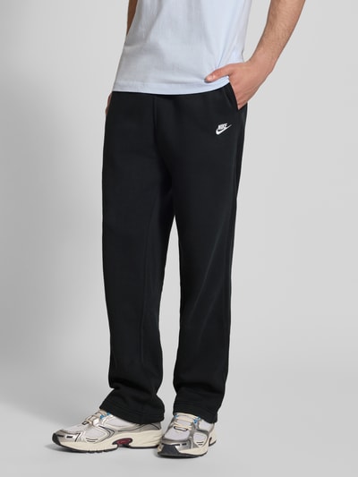 Männermodel trägt schwarze Sweatpants mit Logo-Stitching und Eingrifftaschen von Nike, Baumwoll-Mix, Loose-Fit, Ganzkörperansicht von vorne.