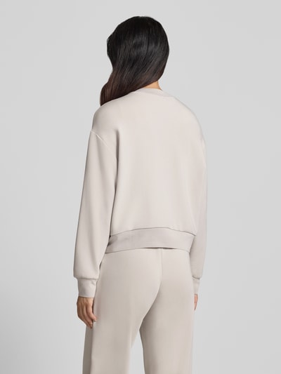 Frauenmodel trägt Sweatjacke mit Label-Print von Armani Exchange in Beige, lockere Passform, glatte Textur, Ganzkörperansicht Rückansicht. Viskose-Mix mit Stretch-Anteil, Zweiwege-Reißverschluss, seitliche Eingrifftaschen.
