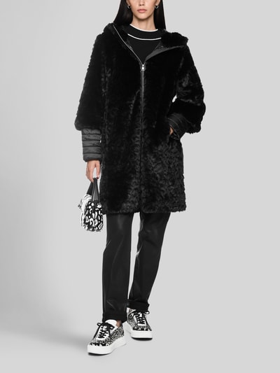 Frauenmodel trägt Mantel aus Kunstfell mit Zweiwege-Reißverschluss von Marc Cain in Schwarz, Regular Fit, Stehkragen, glatte Struktur, Ganzkörperansicht von vorne. Rückenlänge 90 cm, Schulterbreite 43 cm, Brustweite 52 cm, Ärmellänge 63 cm.