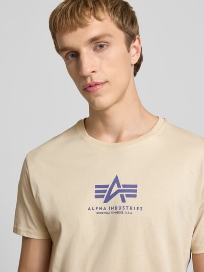 Männermodel trägt T-Shirt mit Logo und Rundhalsausschnitt von Alpha Industries, Reine Baumwolle, Regular-Fit, helle Farbe, Nahaufnahme Oberkörper.