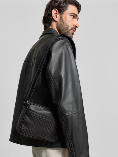 Männermodel trägt Handtasche mit Logo-Muster und Schulterriemen von CK Calvin Klein, Label-Detail, Ganzkörperansicht Rückansicht.