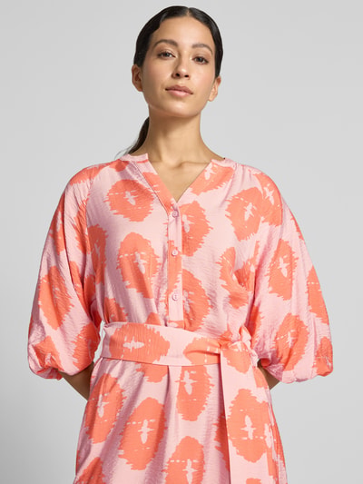 Frauenmodel trägt Knielanges Kleid aus Viskose-Mix von Christian Berg Woman, Muster in Rosa und Orange, Serafino-Ausschnitt, Nahaufnahme Oberkörper.